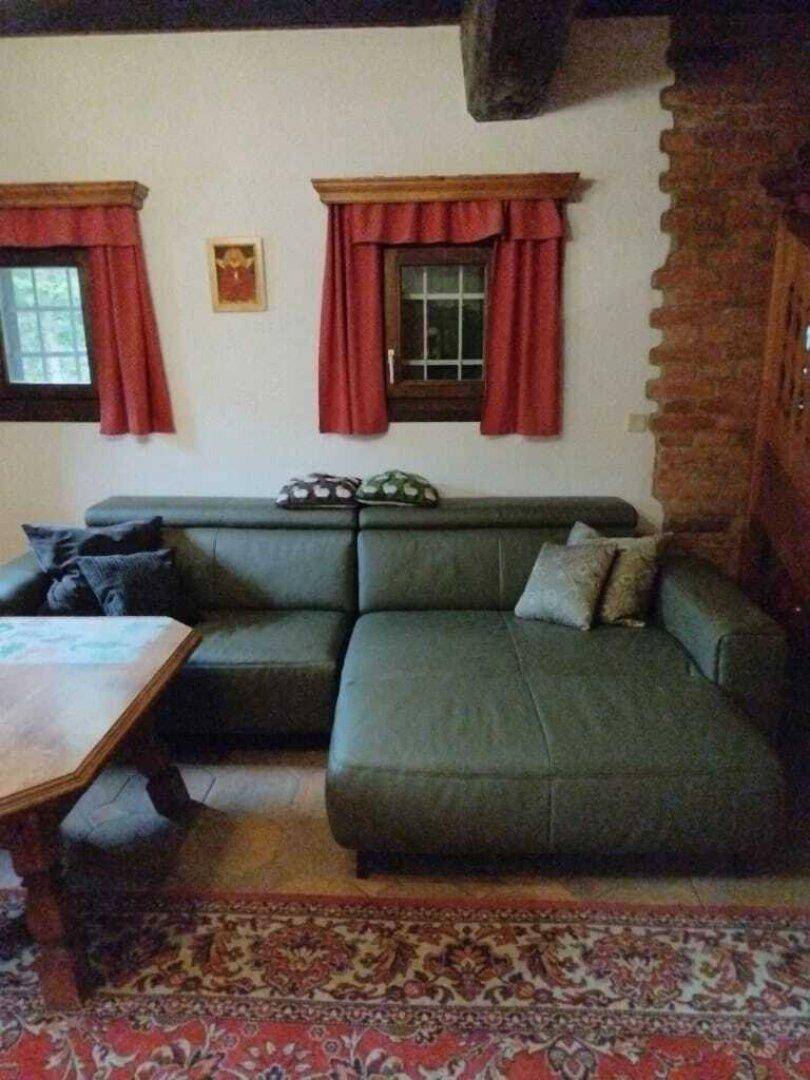 Detailansicht des Ledersofas im rustikalen Wohnzimmer mit kleinen Fenstern und roten Vorhängen.
