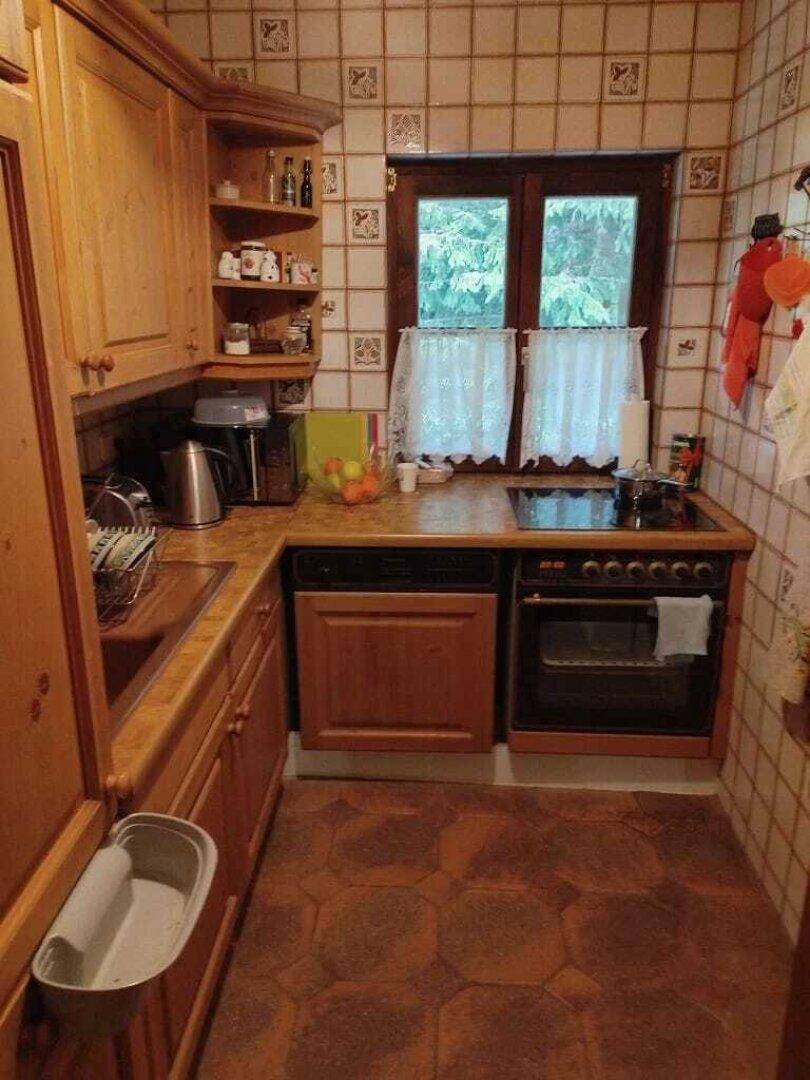 Kleine Küche im Landhausstil mit Holzschränken, Fliesenwand und Fensterblick ins Grüne.