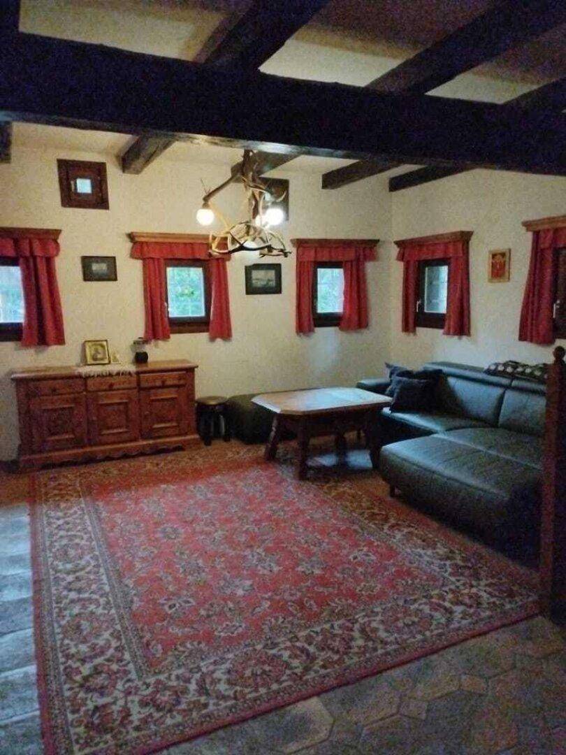 Gemütliches Wohnzimmer im Landhausstil mit Holzbalkendecke, Ledersofa und traditionellem Teppich.