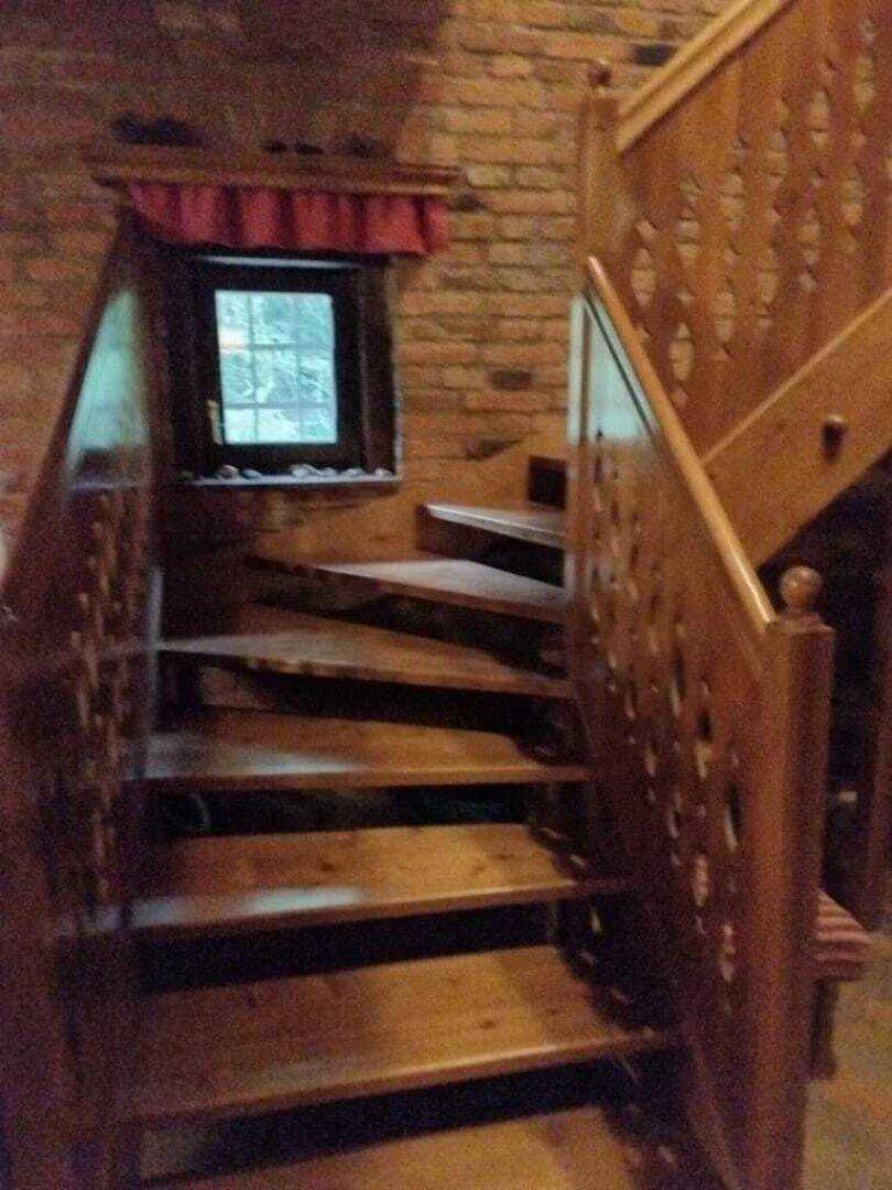 Holztreppe mit kunstvoll geschnitztem Geländer und kleinem Fenster im Treppenhaus.