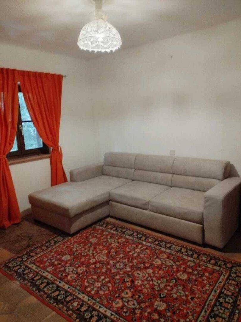 Gemütliches Wohnzimmer mit hellem Ecksofa, rotem Teppich und orangefarbenen Vorhängen.