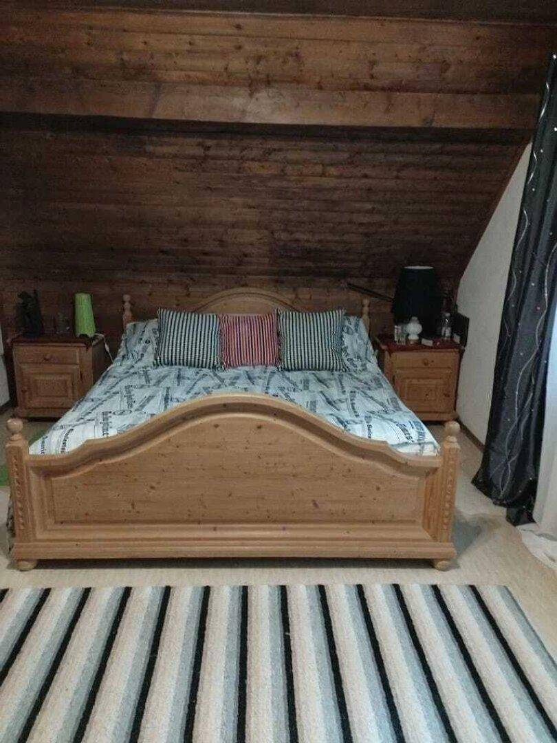 Gemütliches Schlafzimmer im Dachgeschoss mit Holzdoppelbett und gestreiftem Teppich.