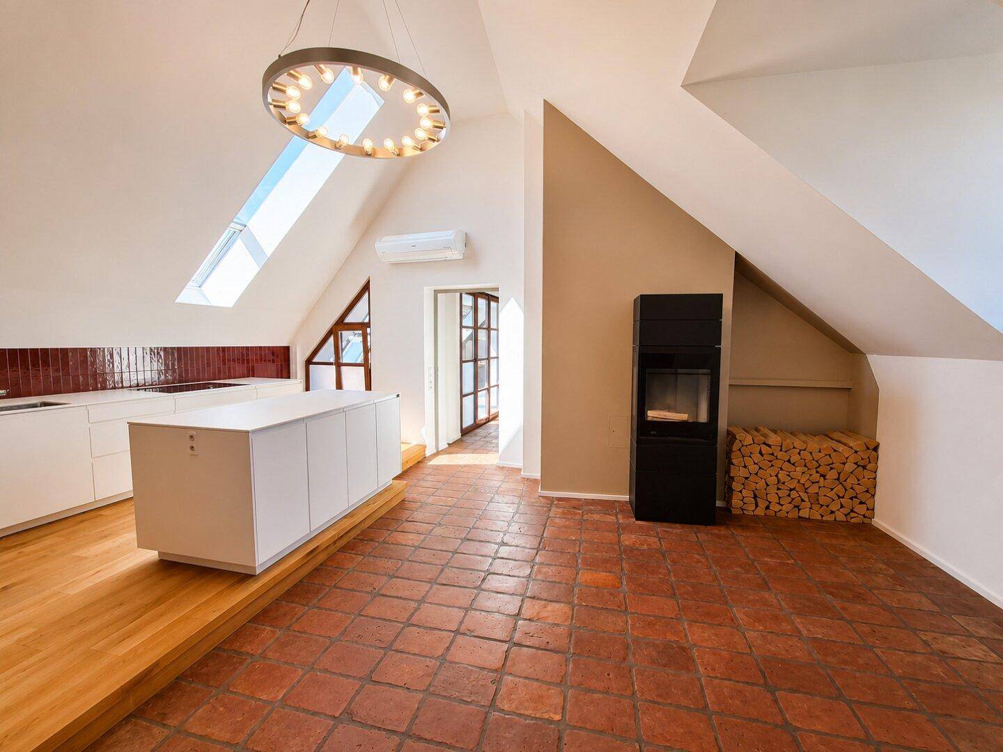 Moderne Küche mit Kochinsel, Terrakottaboden und Kaminofen unter einer Dachschräge.