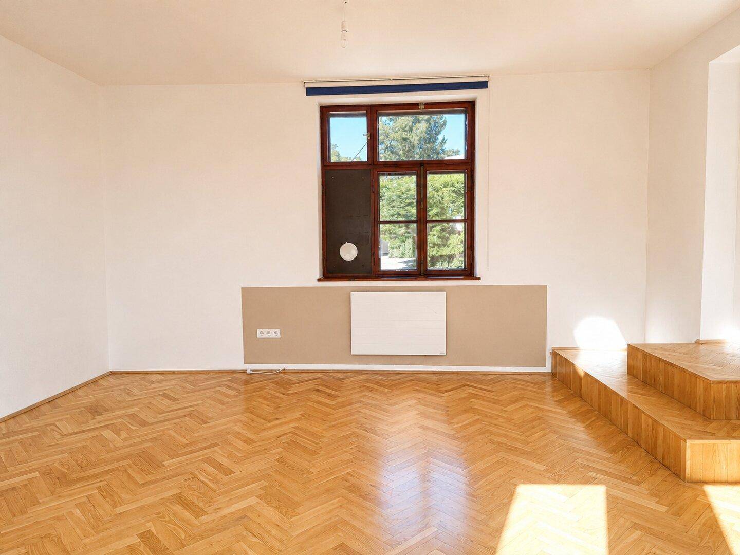 Geräumiges Schlafzimmer mit Fischgrätparkett und großem Fenster, das viel Licht spendet.