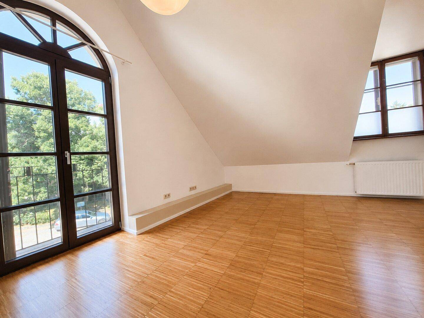 Helles Schlafzimmer mit Holzboden, Dachschräge und französischem Balkon mit Blick ins Grüne.