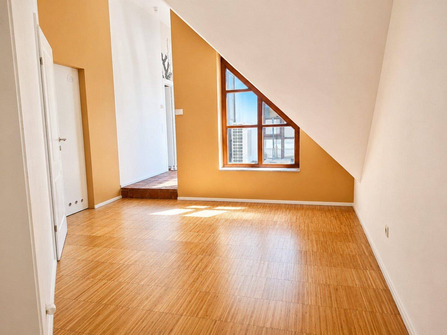 Helles Schlafzimmer mit Holzboden, gelben Wänden und einem dreieckigen Fenster.