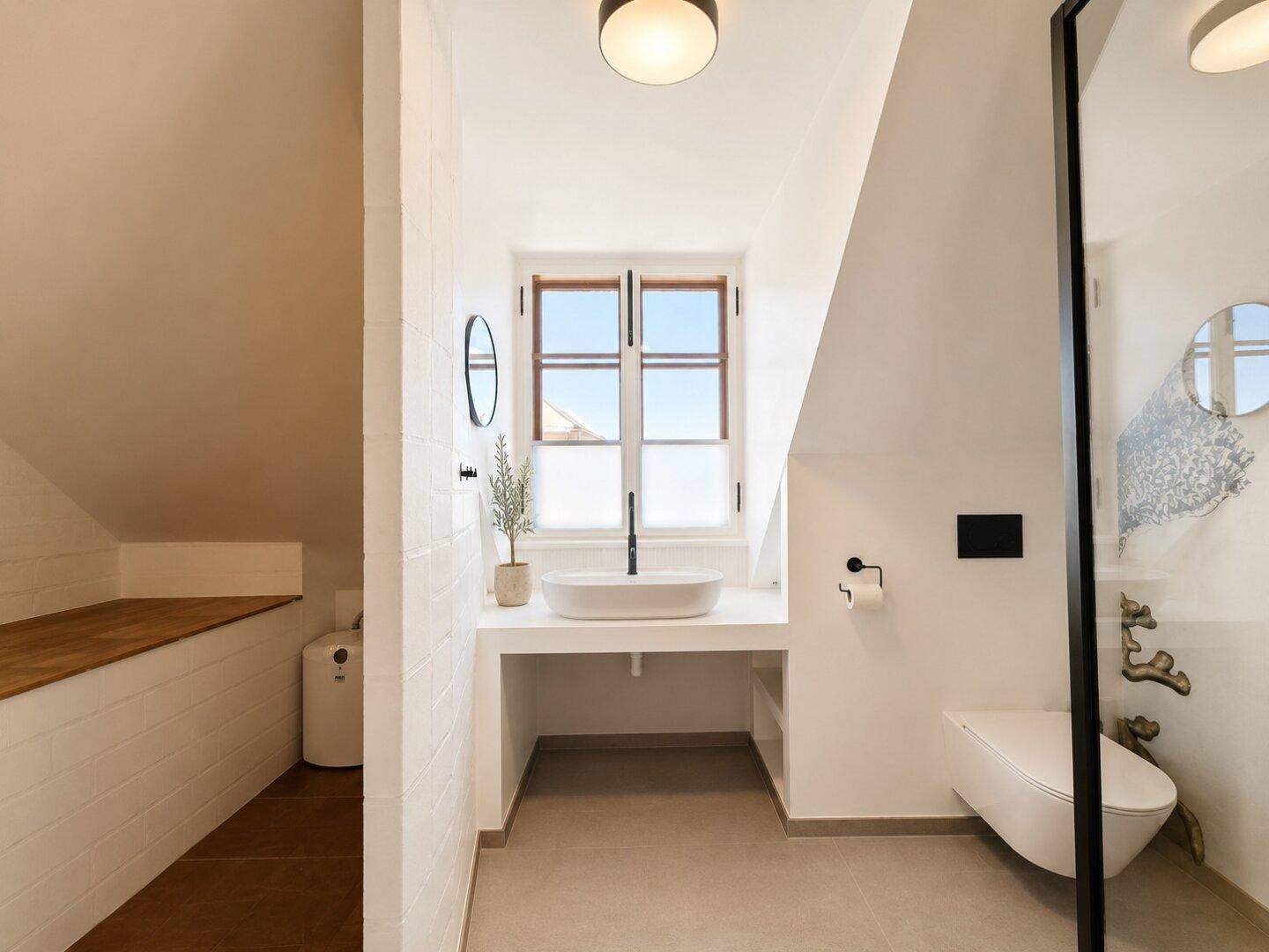 Modernes Badezimmer mit Aufsatzwaschbecken, Wand-WC und Fenster unter einer Dachschräge.