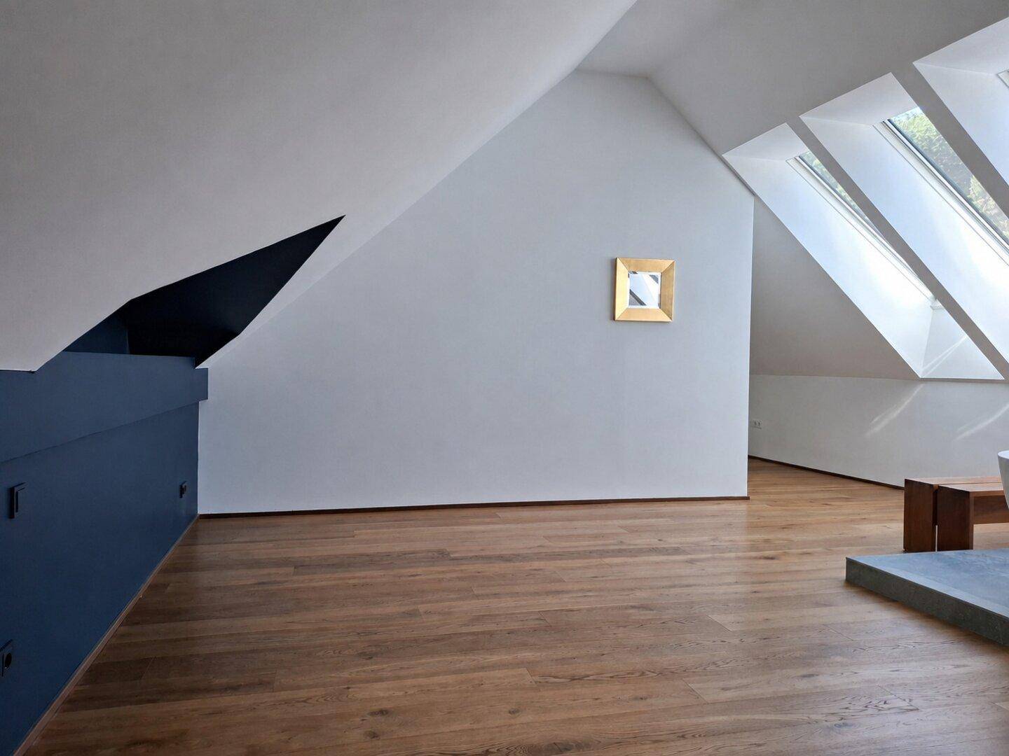 Schlafzimmer mit Holzboden, blauen Wänden und Dachfenstern, die viel Licht hereinlassen.