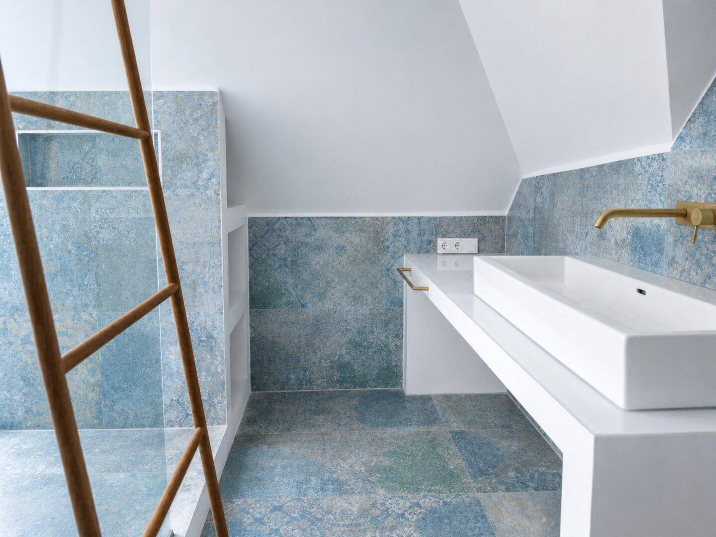 Modernes Badezimmer mit blauen Fliesen, Aufsatzwaschbecken und goldfarbenen Armaturen.
