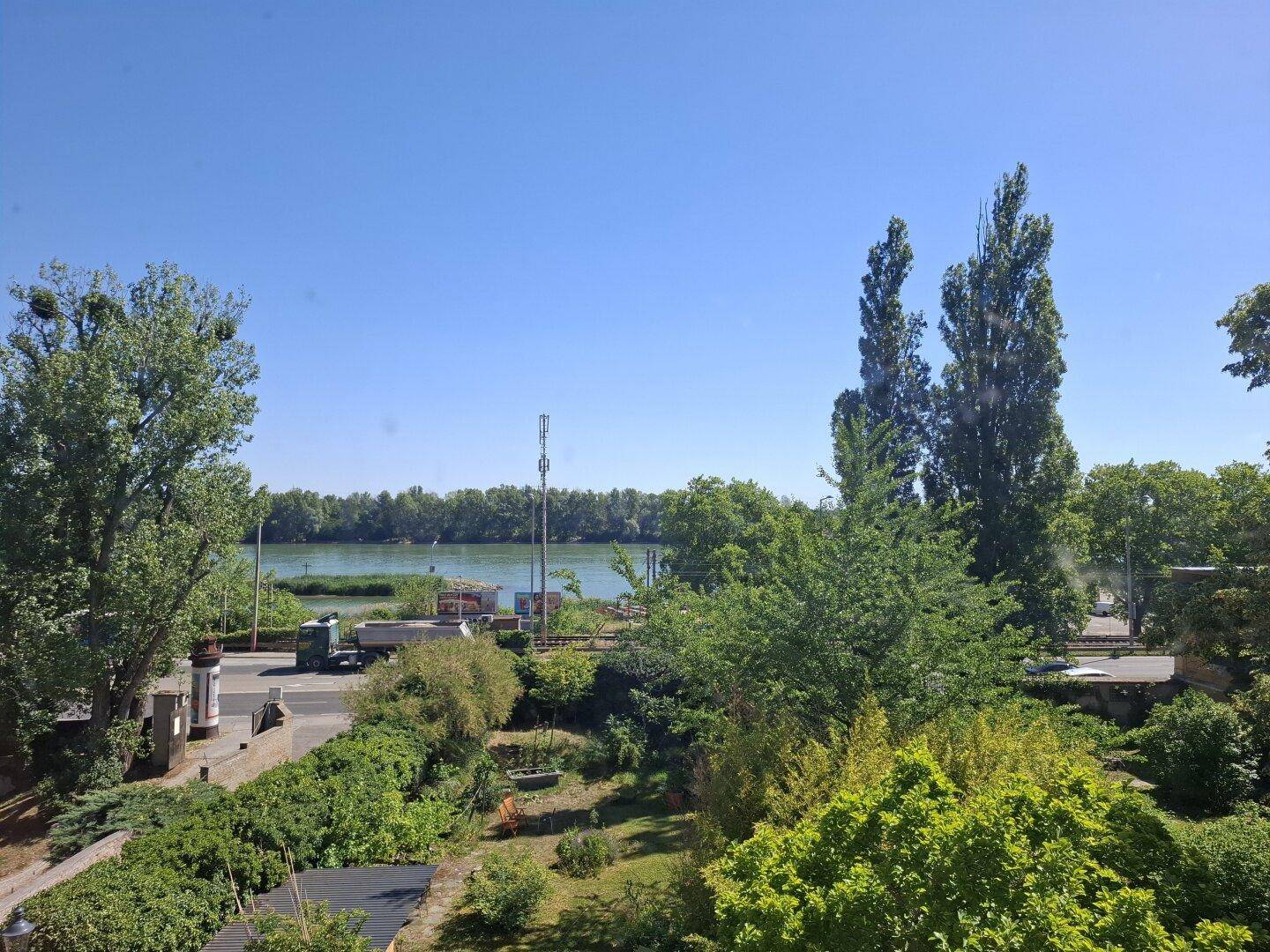 Weitblick auf einen Fluss, umgeben von üppigem Grün und Bäumen unter blauem Himmel.