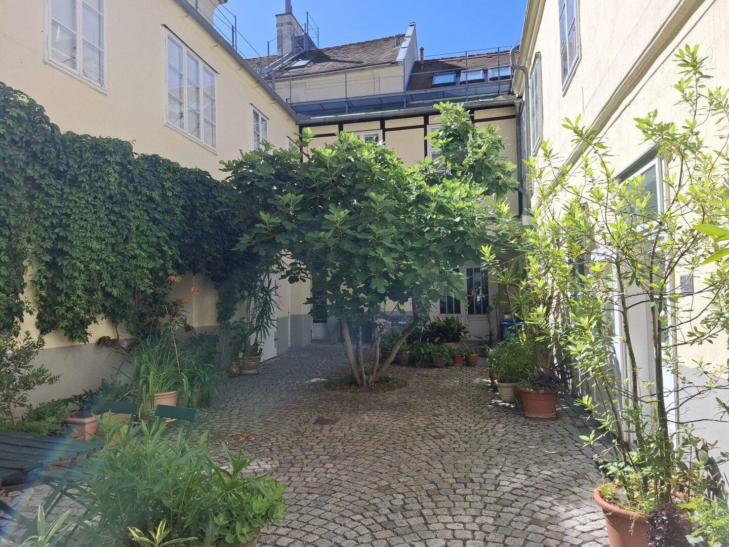 Idyllischer Innenhofgarten mit üppigem Grün, Kopfsteinpflaster und Sitzgelegenheiten, umgeben von historischen Gebäuden.