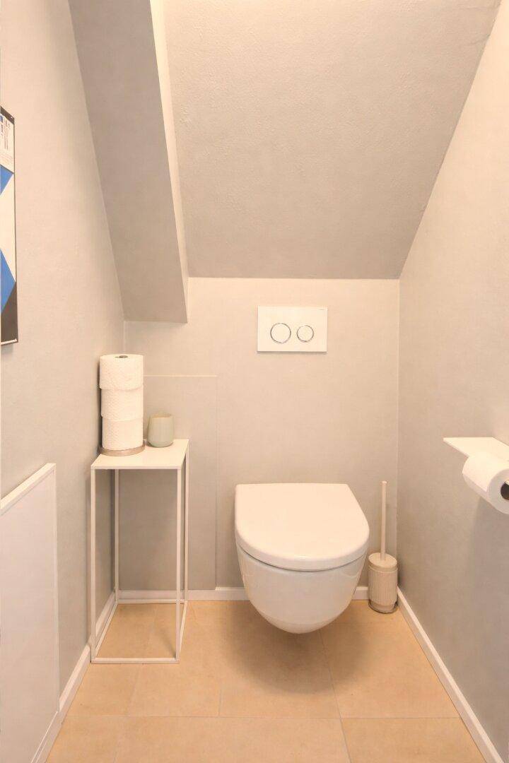 Modernes Gäste-WC mit Wand-WC und hellem Fliesenboden unter einer Dachschräge.