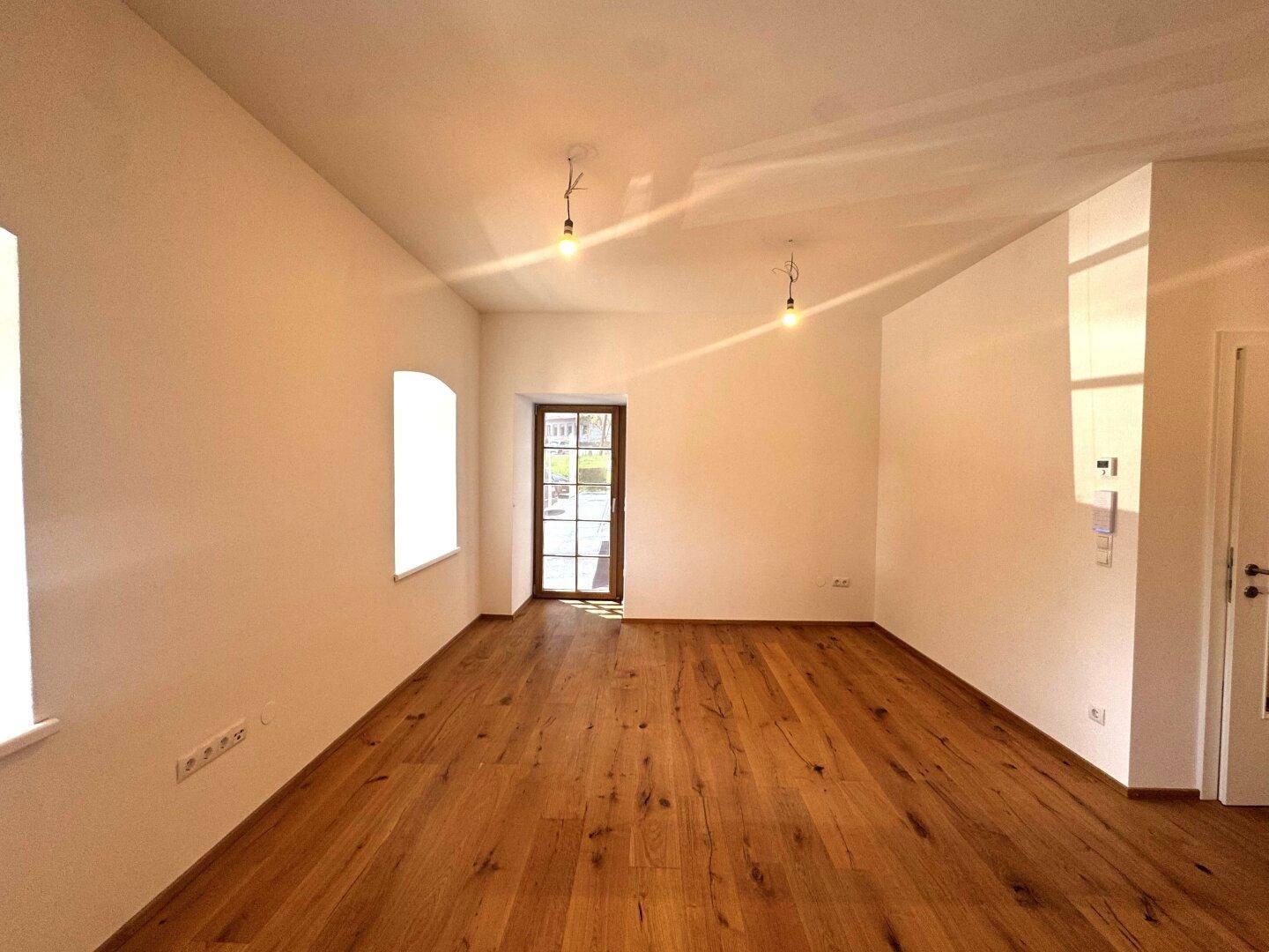 Geräumiger, heller Raum mit Holzboden und einer Tür mit Glasausschnitt, die ins Freie führt.