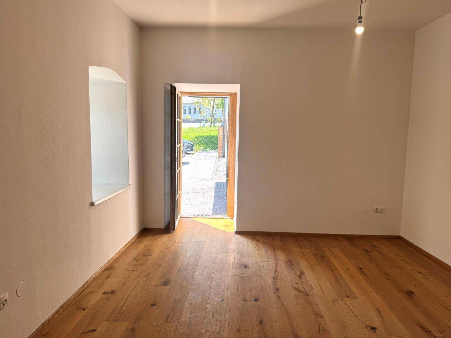 Heller Raum mit Holzboden und einer offenen Tür, die ins Freie führt.