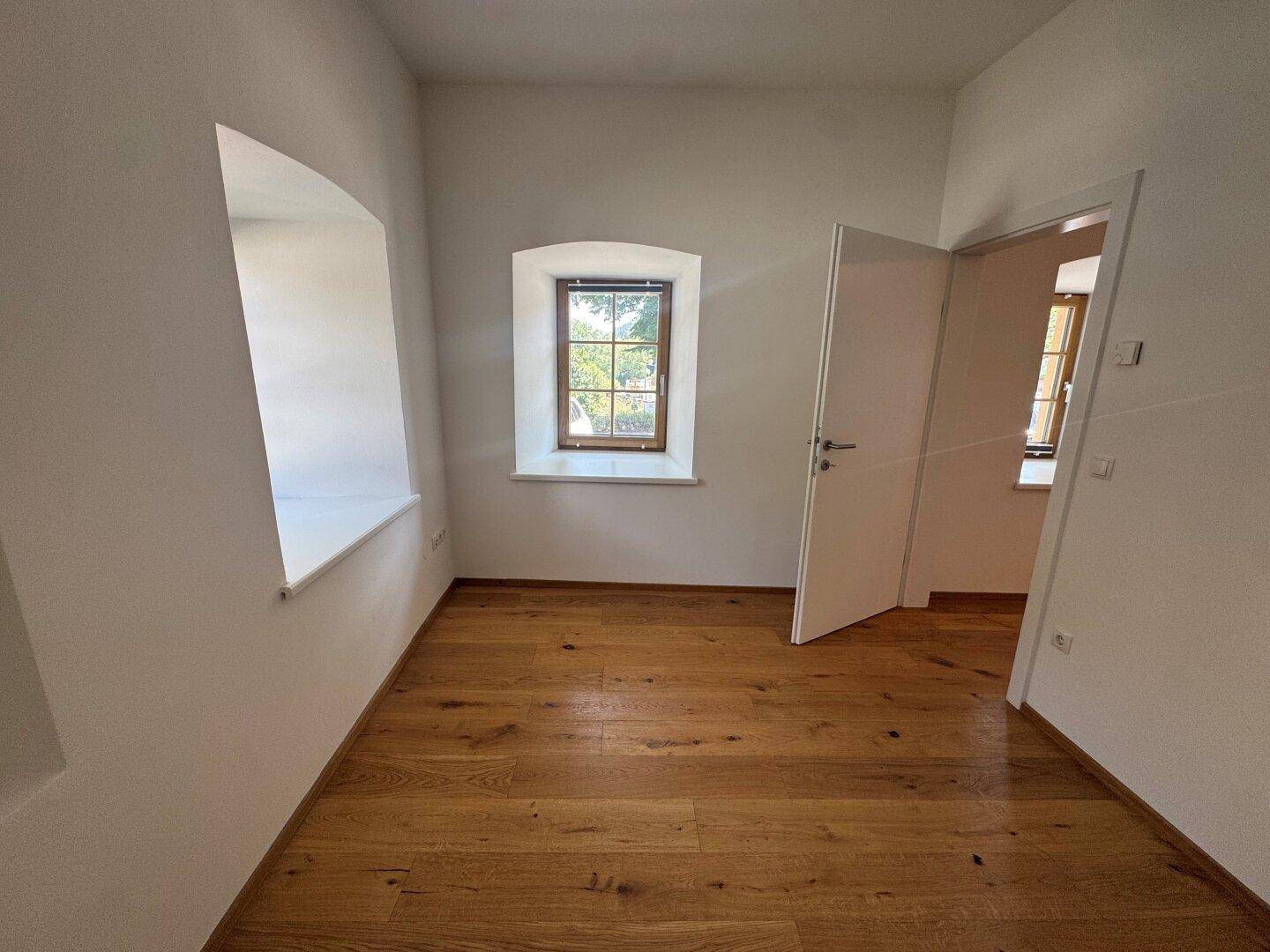 Helles Zimmer mit Holzboden und einem Fenster, das einen Blick nach draußen bietet.