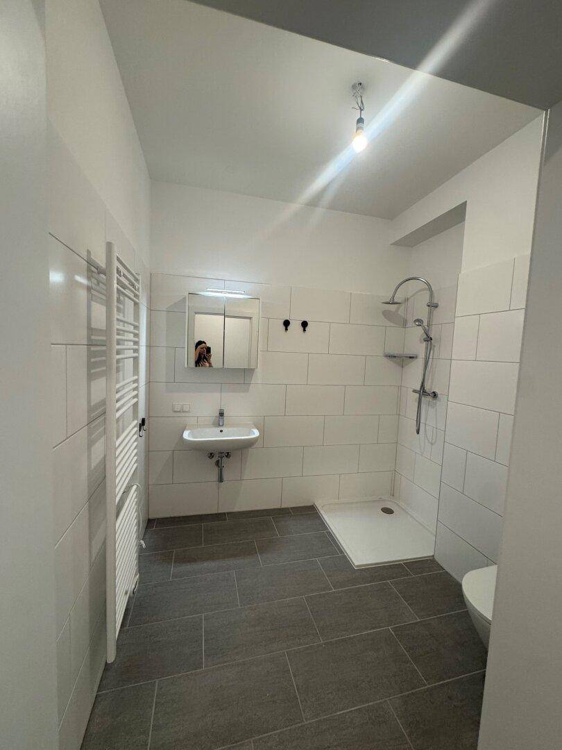 Modernes Badezimmer mit weißen Fliesen, grauen Bodenfliesen und einer ebenerdigen Dusche.