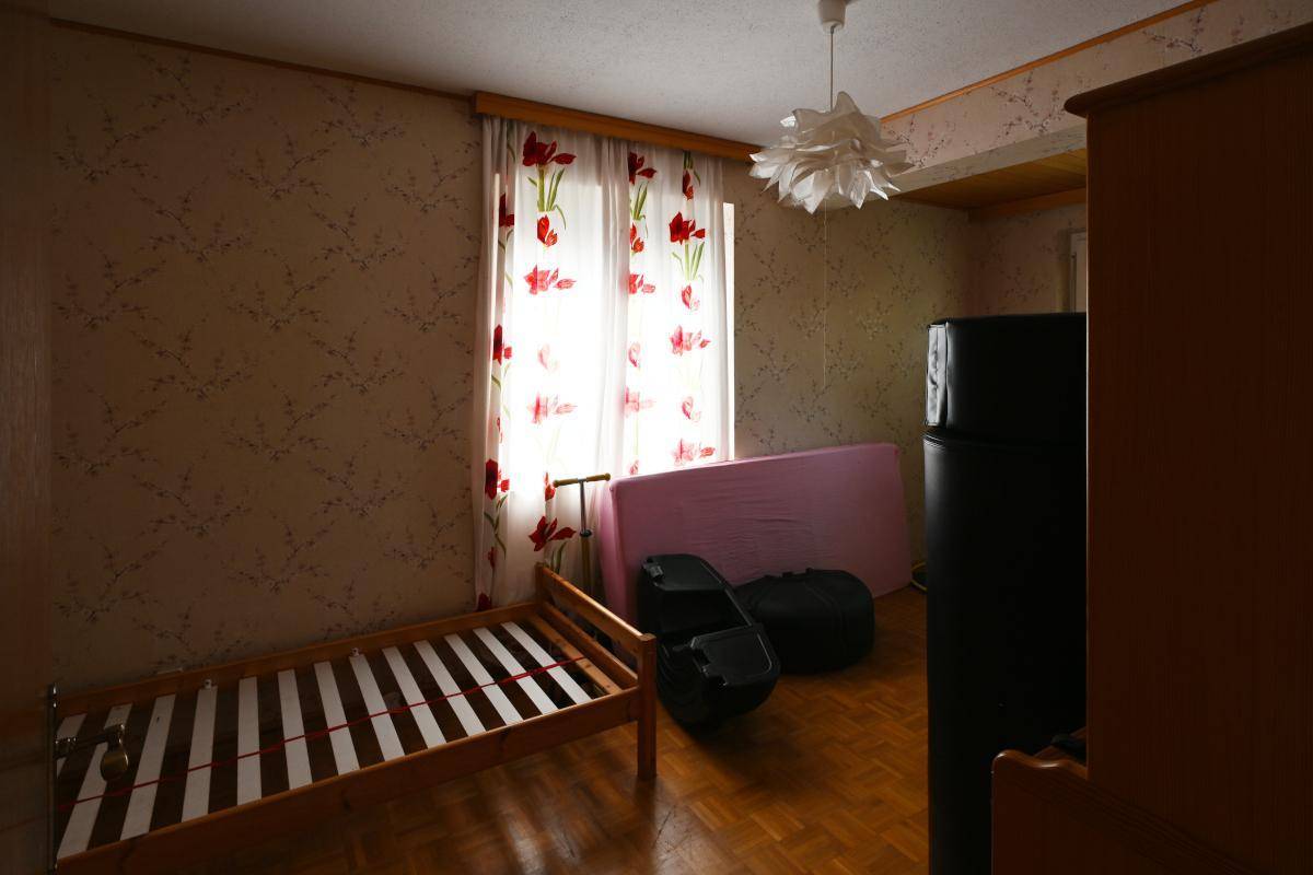 Helles Schlafzimmer mit Holzbett, Parkettboden und einem Fenster mit floralen Vorhängen.