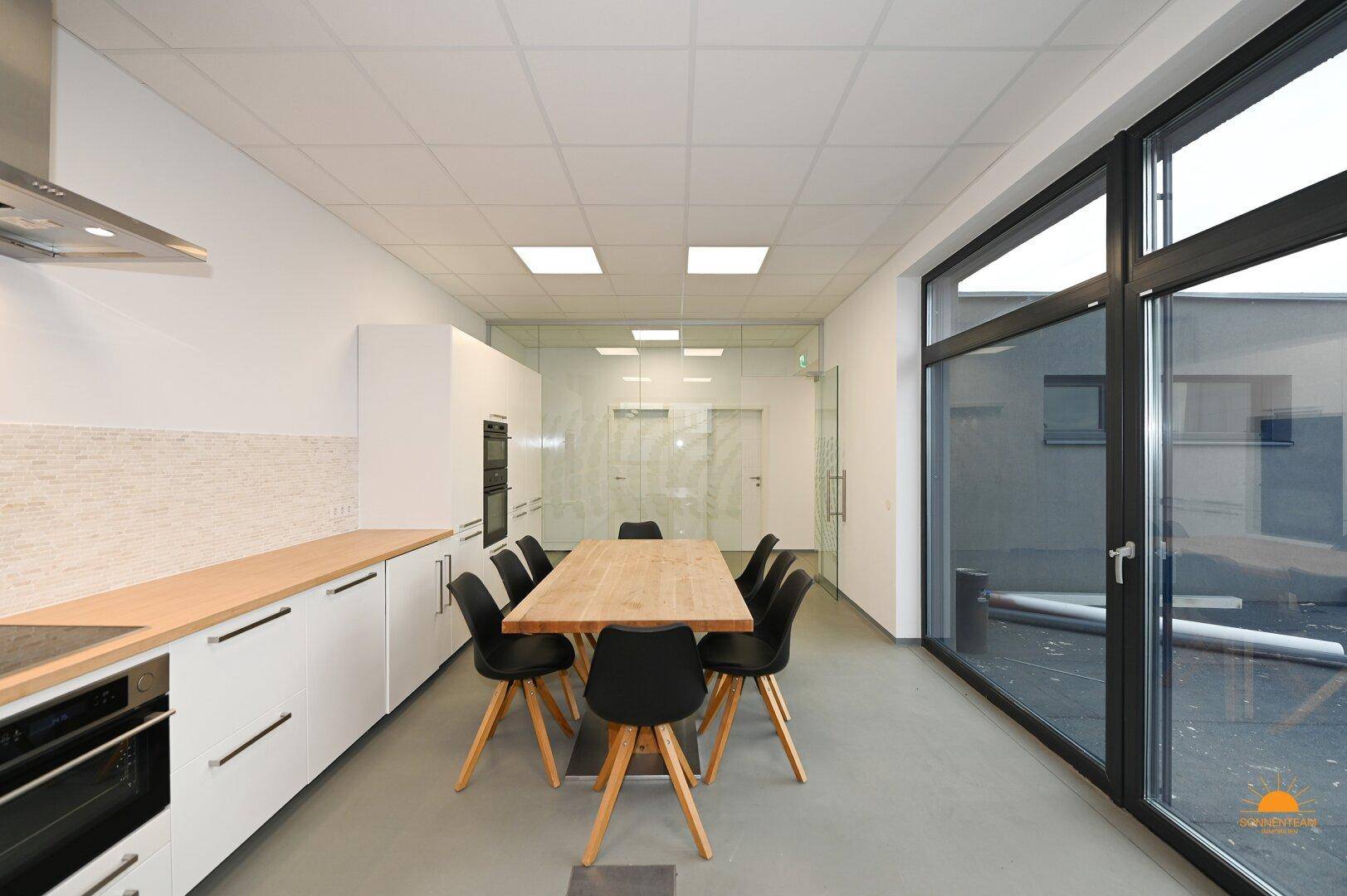 Geräumige, moderne Küche mit Essbereich, weißen Schränken und großen Fenstern, die viel Licht hereinlassen.