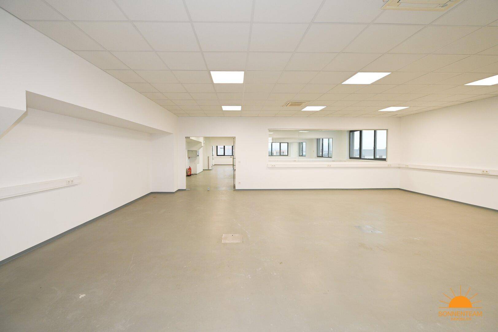Großer, offener Bürobereich mit hellen Wänden und Fenstern, die viel natürliches Licht hereinlassen.