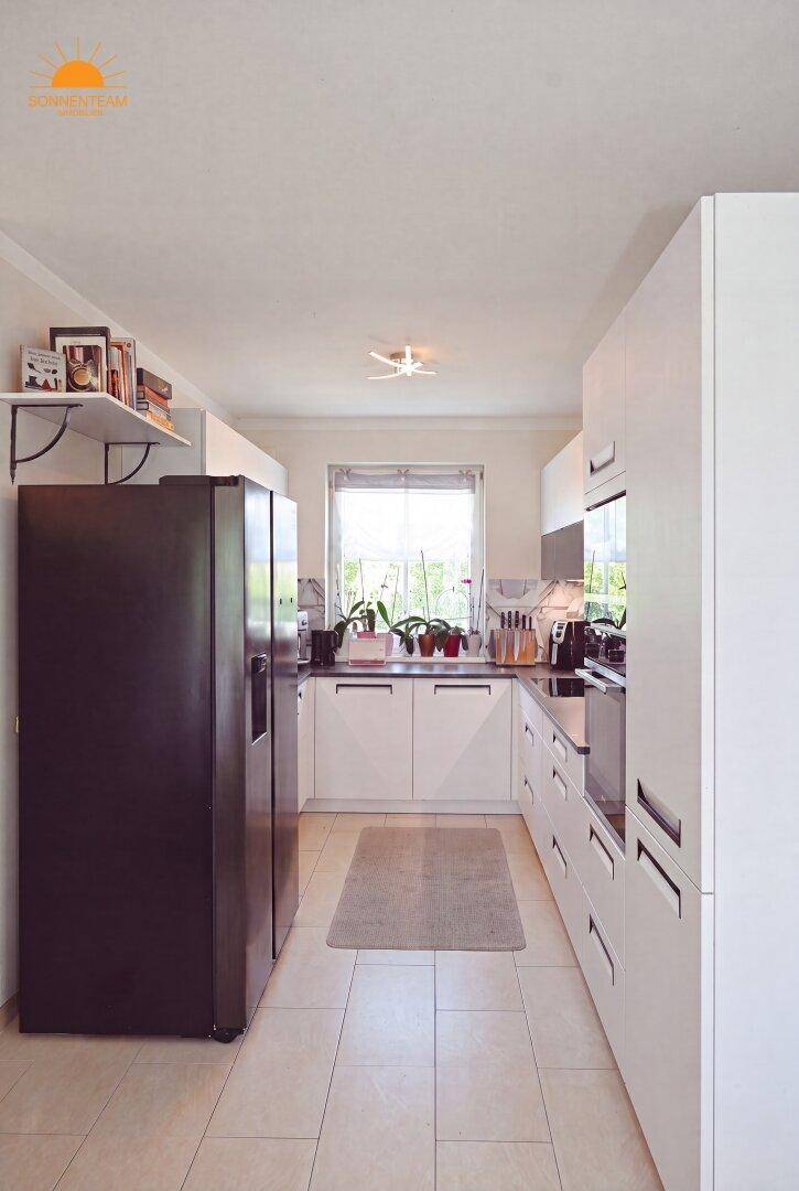 Moderne Küche mit weißen Schränken, großem Kühlschrank und Fenster.