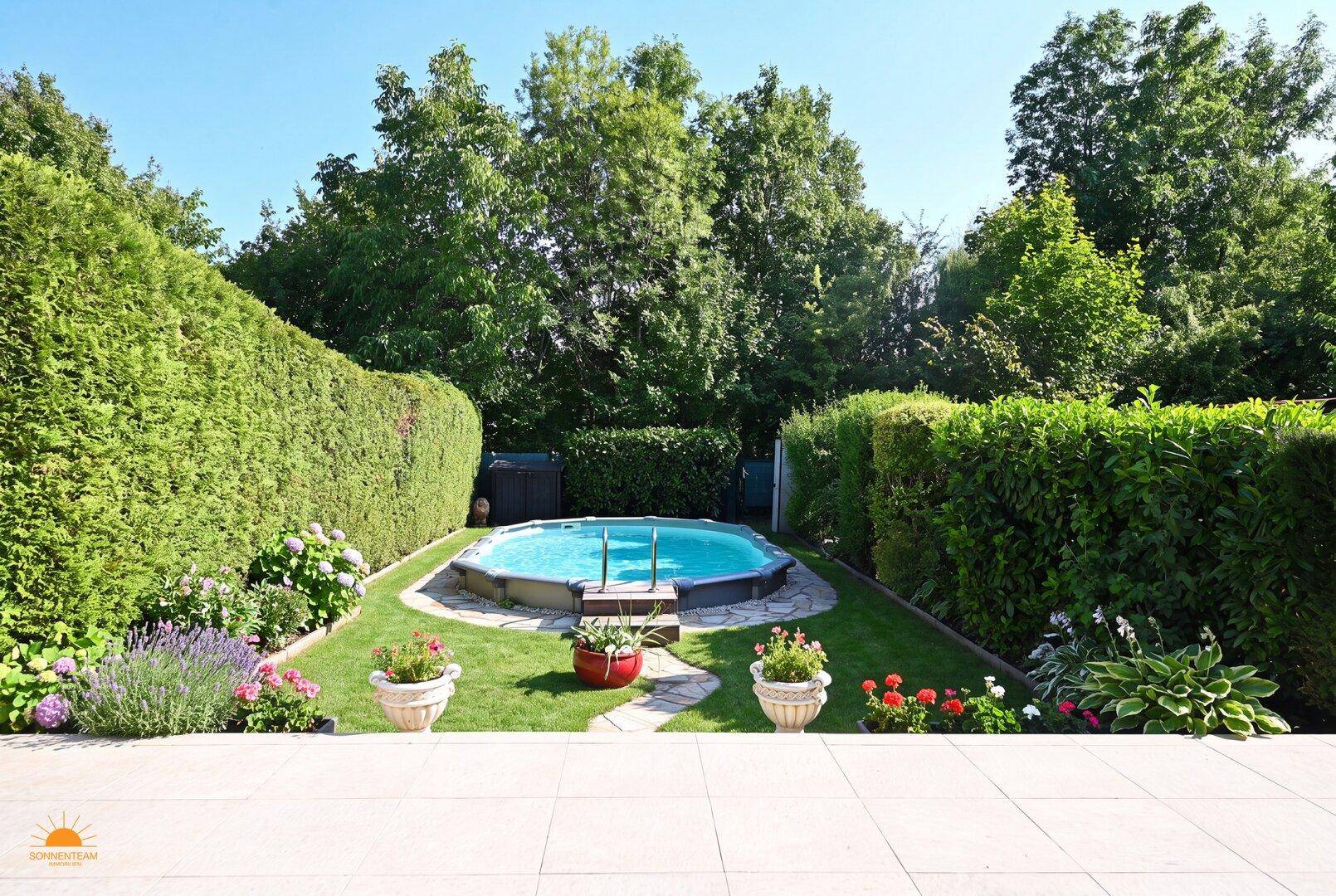 Großer, gepflegter Garten mit Rasenfläche, Swimmingpool und hohen Hecken.