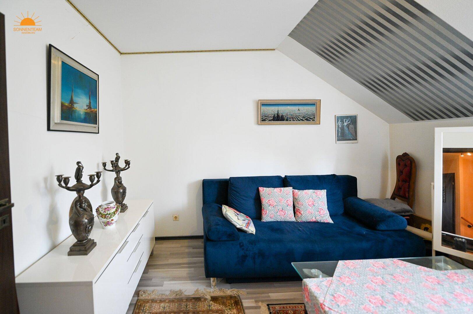Gemütliches Wohnzimmer mit blauem Sofa, Kunstwerken und schräger Decke im Dachgeschoss.