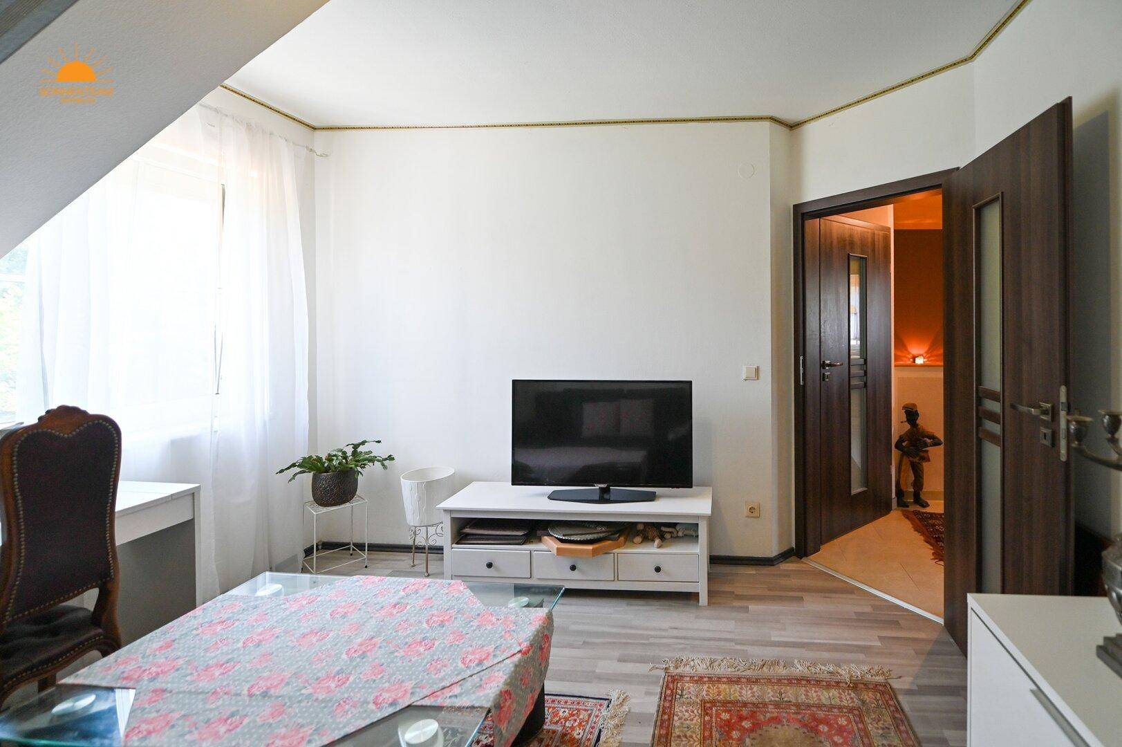 Helles Zimmer mit Fernseher, Schreibtisch und Blick ins Grüne durch das Fenster.