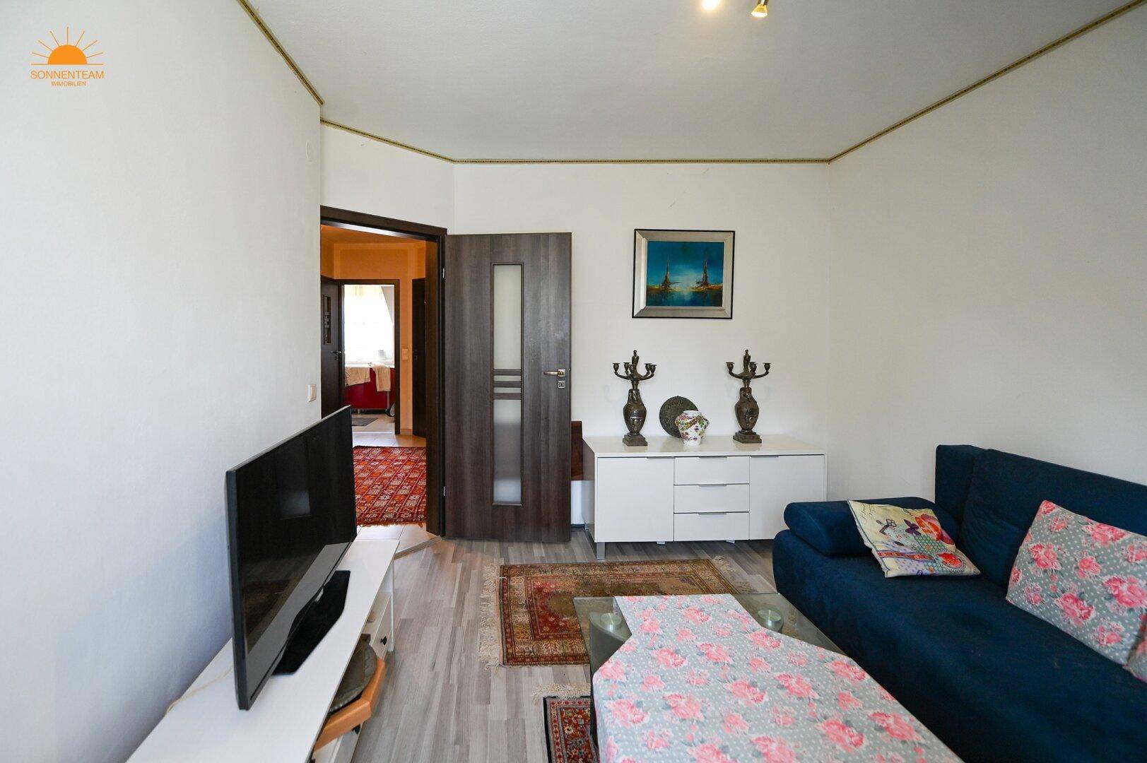 Wohnzimmer mit blauem Sofa, Fernseher und dekorativen Elementen.