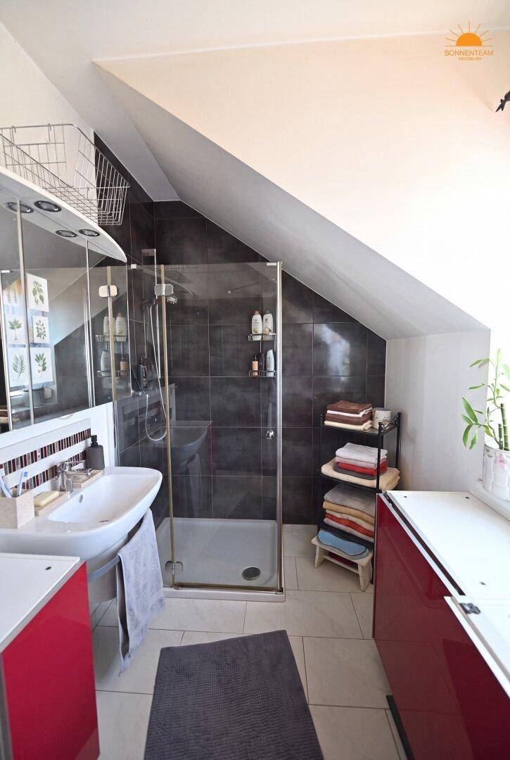 Modernes Badezimmer im Dachgeschoss mit Dusche, Waschbecken und dunklen Fliesen.