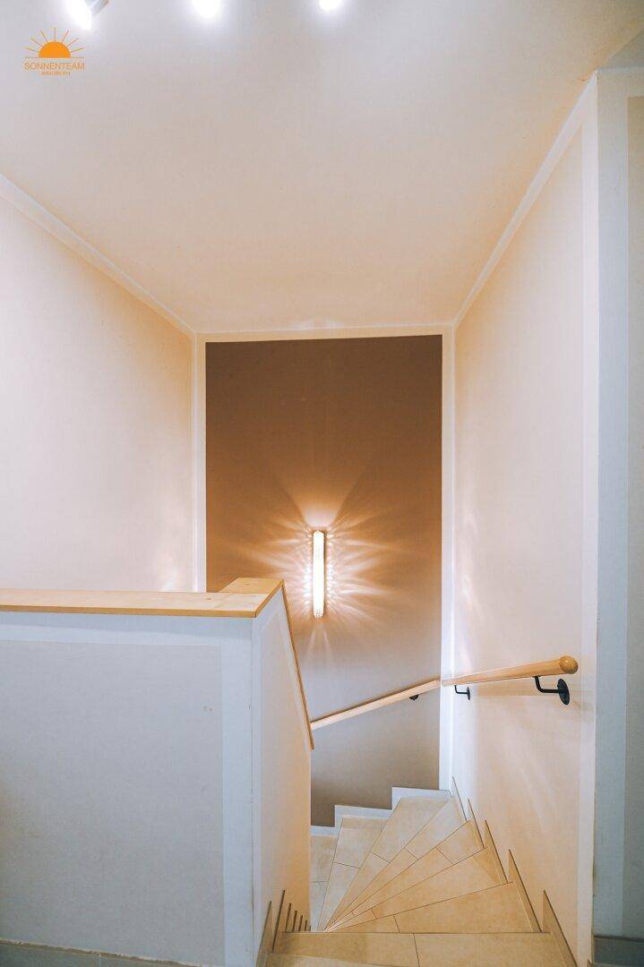 Heller Treppenaufgang mit Holzgeländer und indirekter Beleuchtung an der Wand.