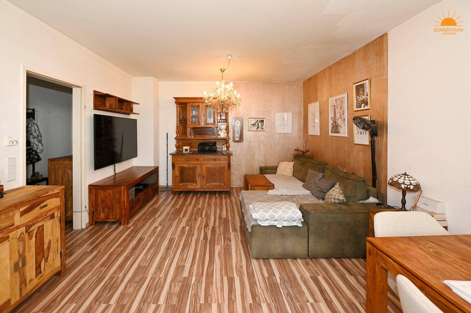 Geräumiger Wohnbereich mit Holzboden, bequemer Couch und einem TV-Möbel aus dunklem Holz.