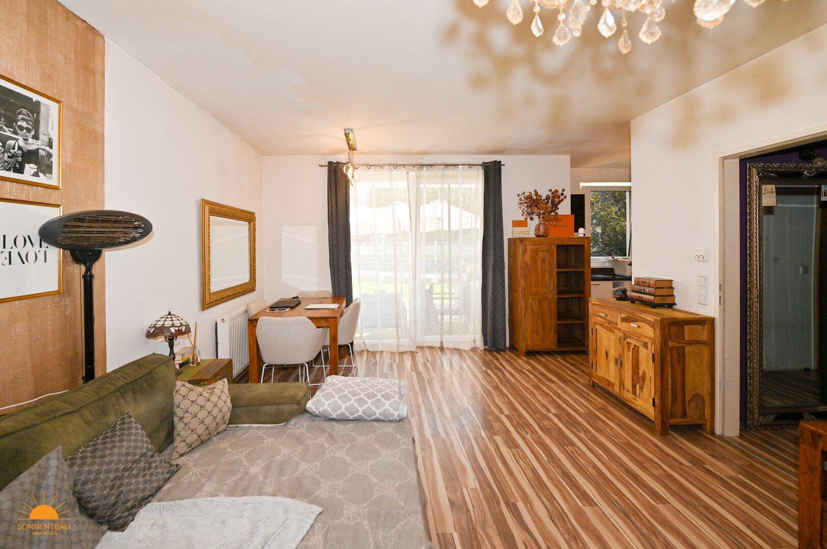 Heller Wohnbereich mit Holzboden, Sofa und Esstisch, mit Blick auf den Außenbereich.