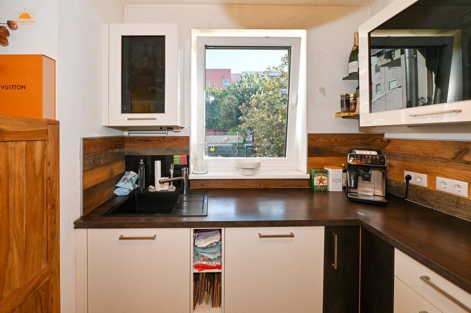Helle Küche mit Spülbecken unter dem Fenster, Holzakzenten und modernen Schränken.