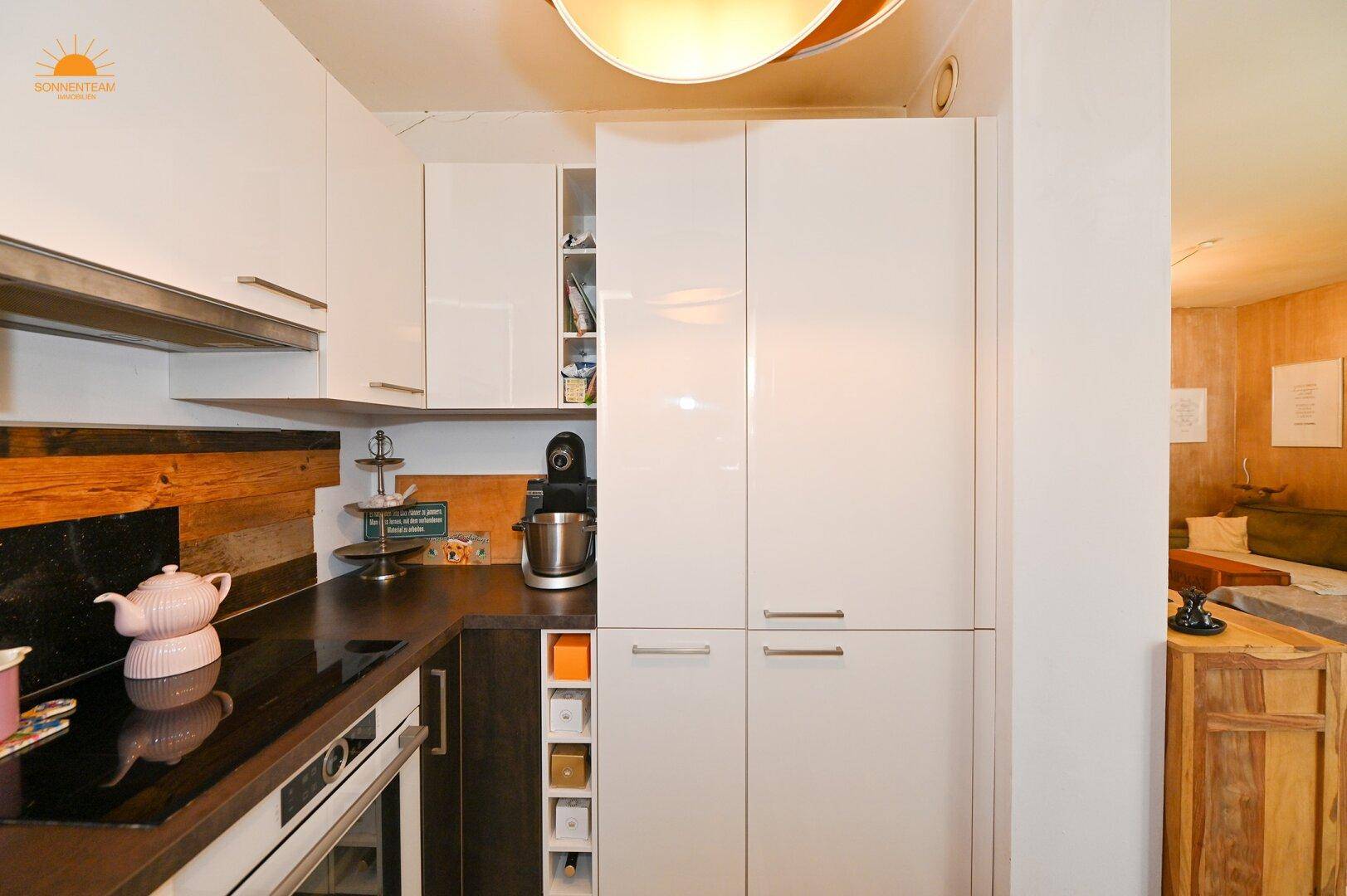 Funktionale Küche mit weißen Hochglanzschränken, integriertem Backofen und viel Stauraum.
