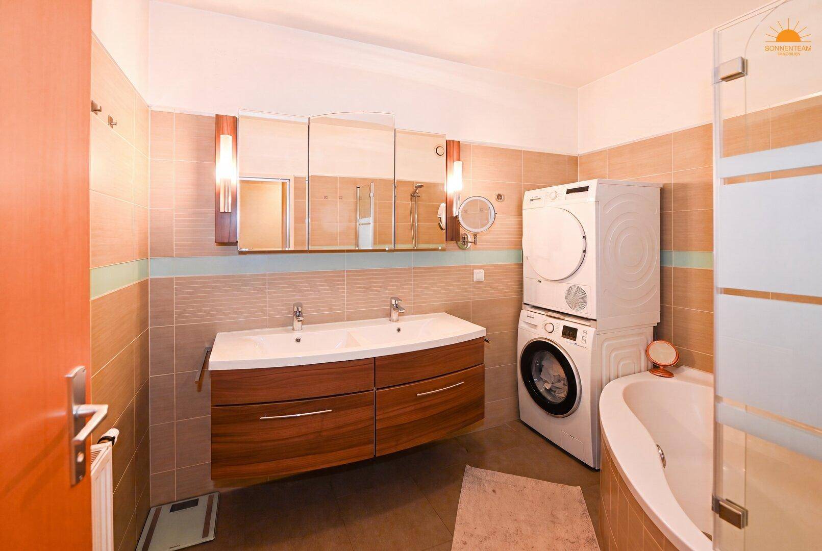 Modernes Badezimmer mit Doppelwaschbecken, Badewanne und integrierter Waschmaschine und Trockner.