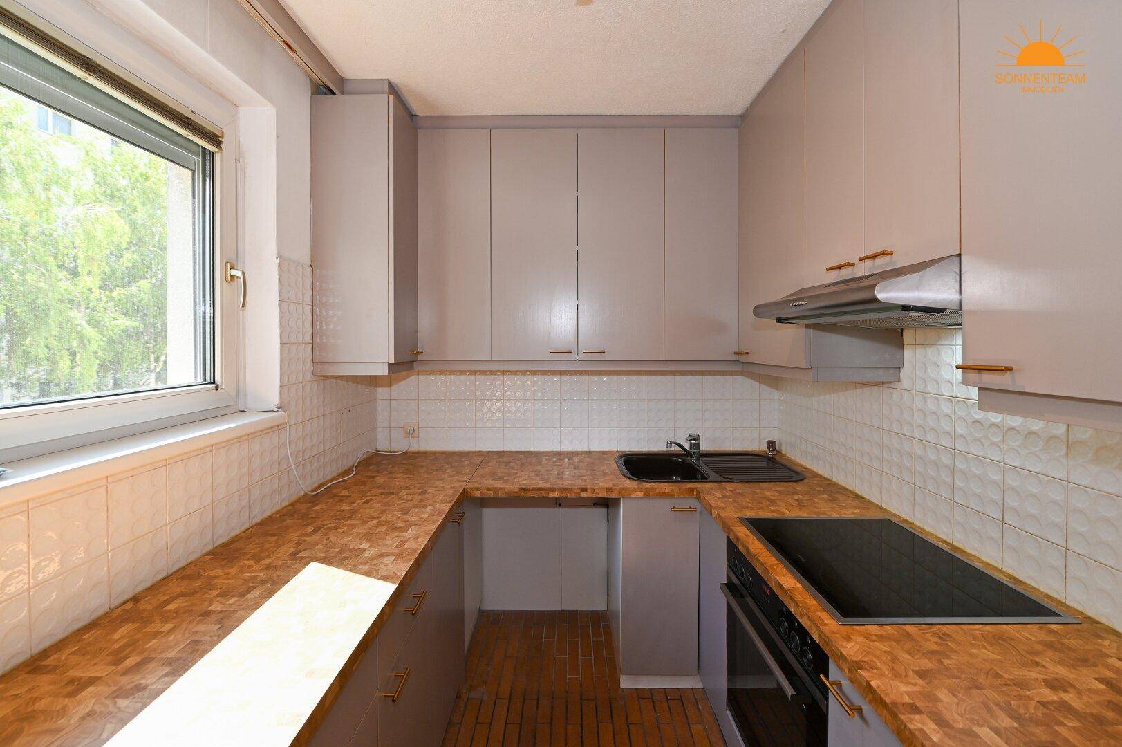 Helle Küche mit grauen Schränken, Holz-Arbeitsplatten und Fensterblick ins Grüne.