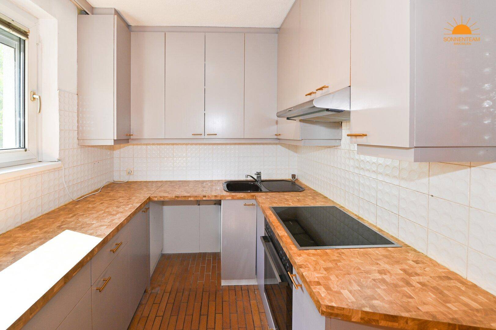 Funktionale Küche mit U-förmiger Arbeitsplatte, grauen Schränken und Fenster für Tageslicht.