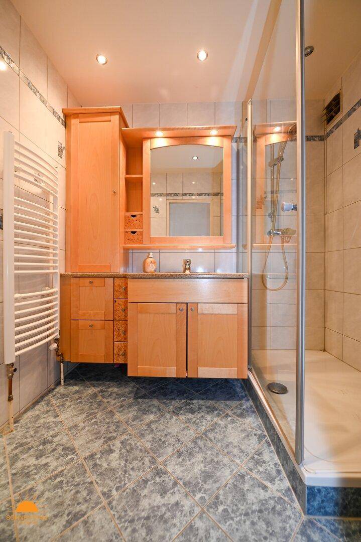 Badezimmer mit Holzmöbeln, Duschkabine und beheiztem Handtuchhalter.