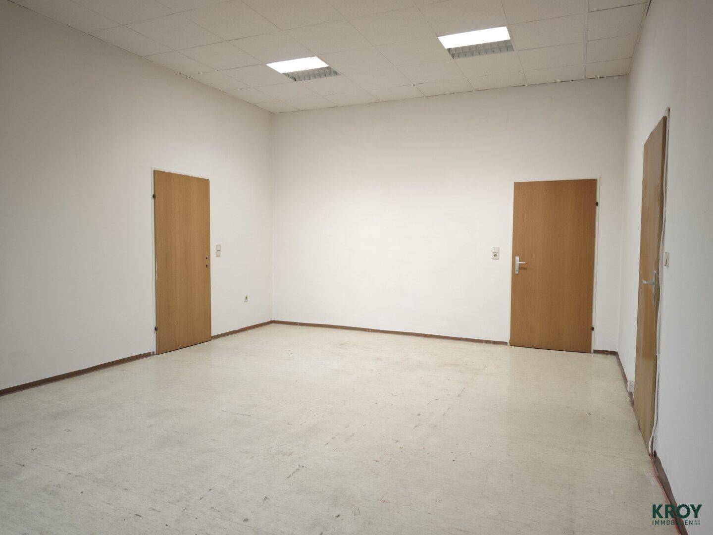 Leerer Raum mit drei Holztüren und einer abgehängten Decke mit Leuchten.