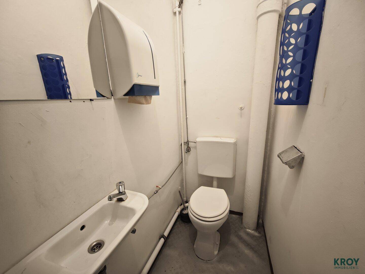 Kleine Toilette mit Waschbecken, WC und Papierhandtuchspender in einfacher Ausführung.
