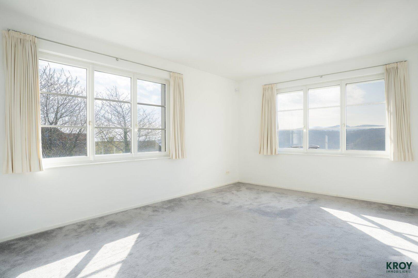 Helles Schlafzimmer mit Teppichboden und großen Fenstern, die einen weiten Blick bieten.