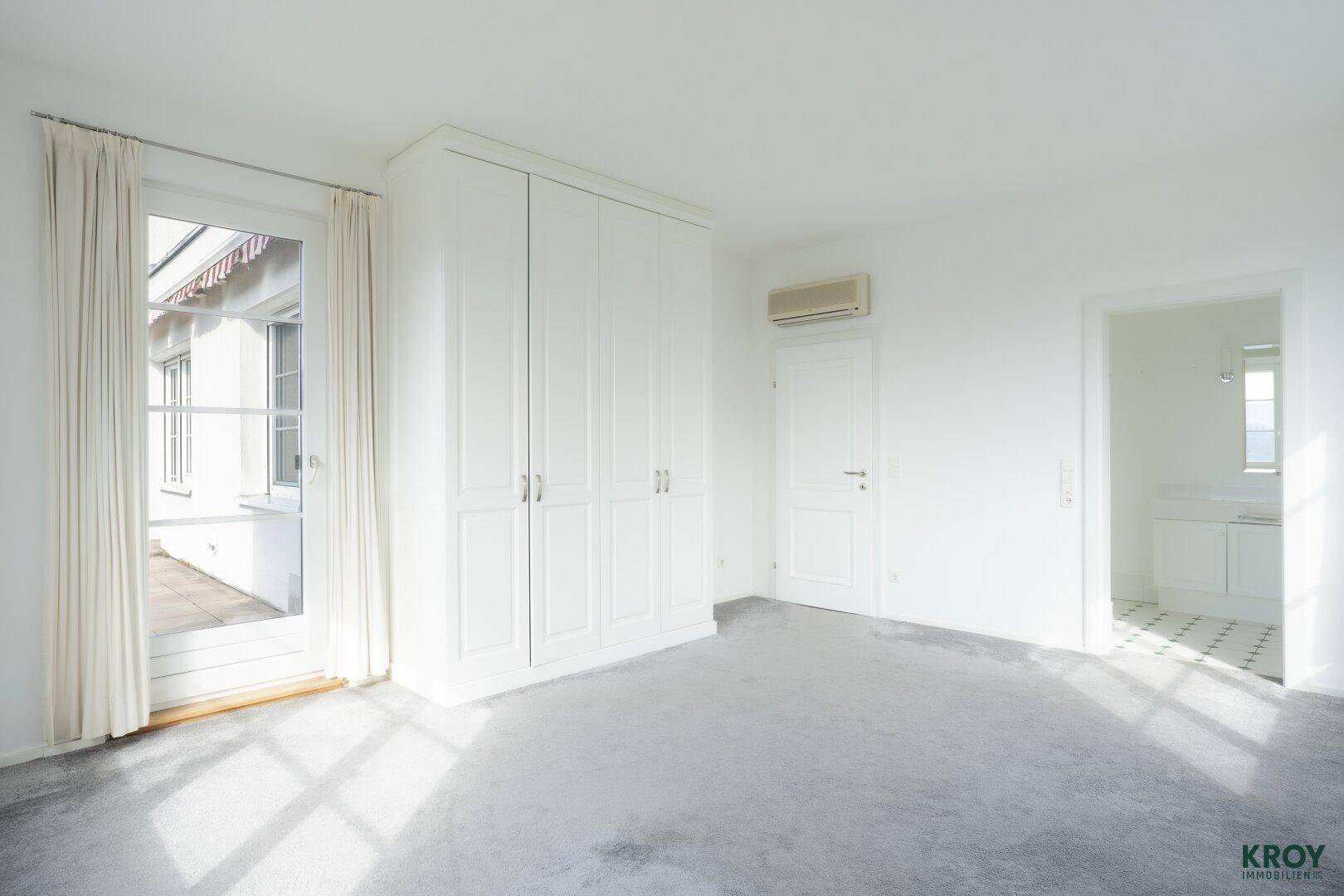Helles Schlafzimmer mit Einbauschränken, Teppichboden und Zugang zu einem Balkon.