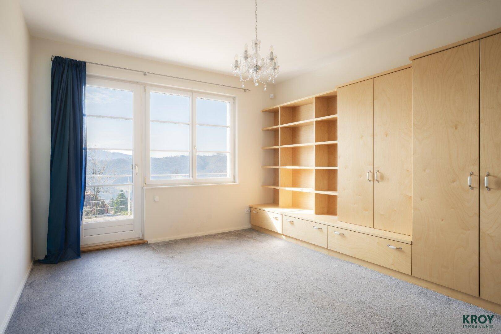 Helles Schlafzimmer mit Teppichboden, Einbauschränken und Zugang zu einem Balkon.