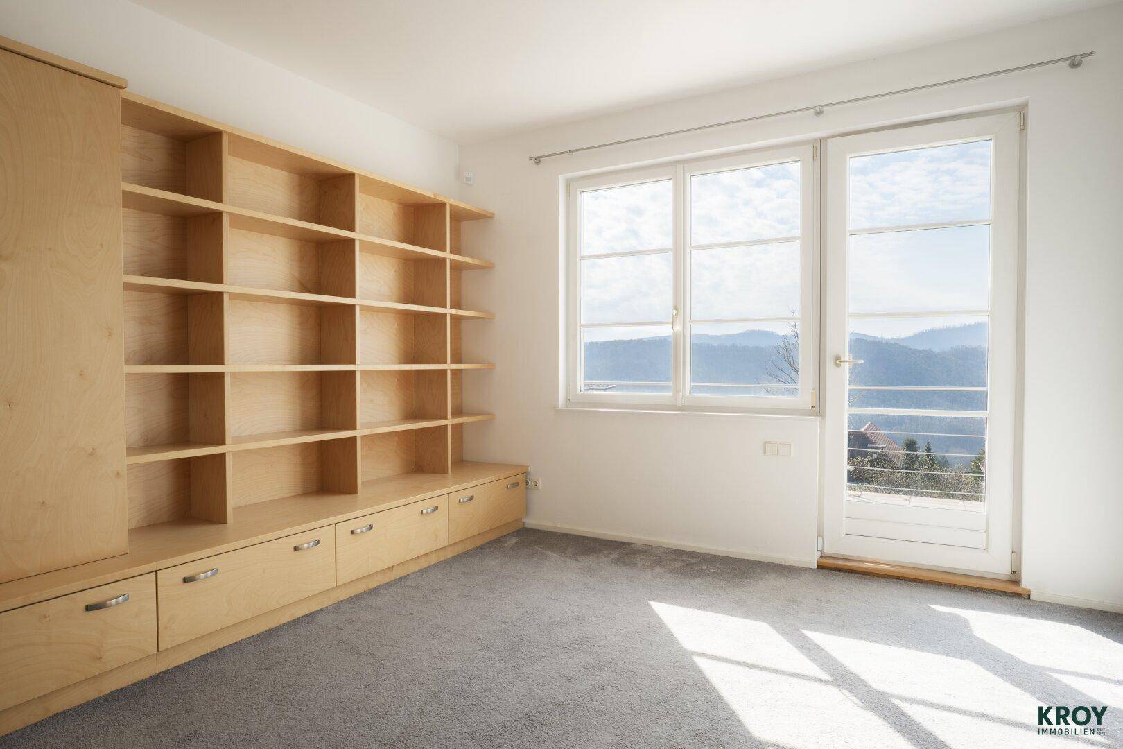 Helles Schlafzimmer mit Teppichboden, Einbauschränken und Zugang zu einem Balkon.