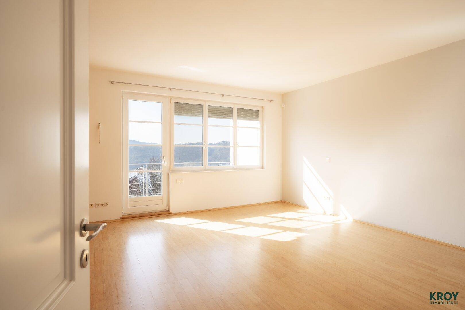 Heller Raum mit Holzboden und Zugang zu einem Balkon, ideal als Wohn- oder Gästezimmer.