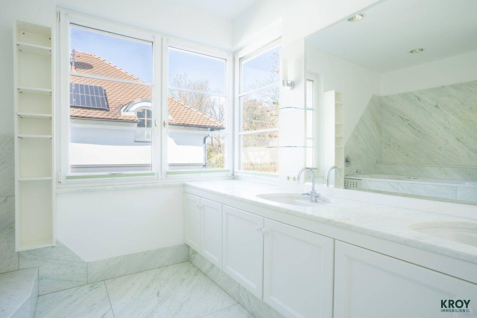 Luxuriöses Badezimmer mit Marmoroberflächen, Doppelwaschbecken und großen Fenstern.