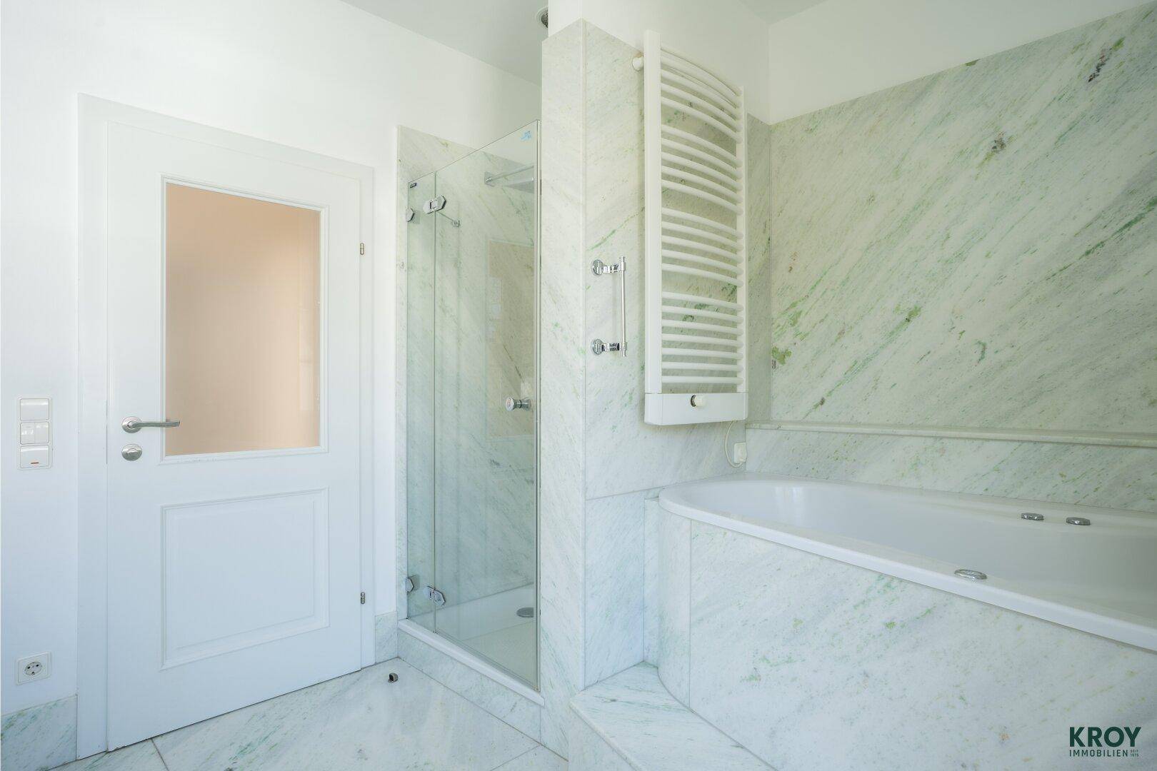 Elegantes Badezimmer mit Marmorfliesen, Badewanne, Duschkabine und beheiztem Handtuchhalter.