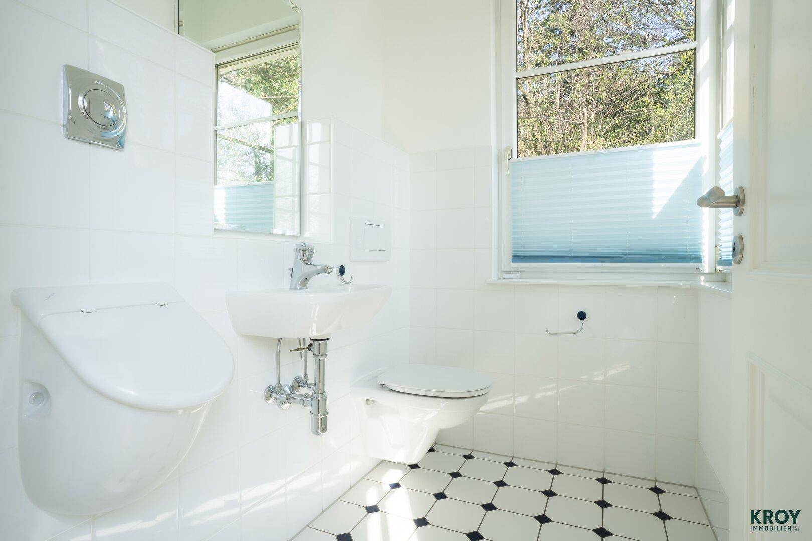 Modernes Gäste-WC mit weißen Fliesen, kleinem Waschbecken und Fenster.