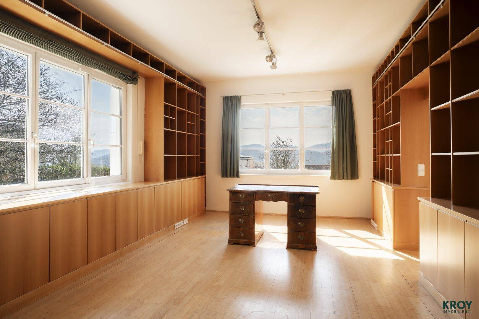 Helles Arbeitszimmer mit Einbauregalen aus Holz, Schreibtisch und weitem Blick auf die Landschaft.