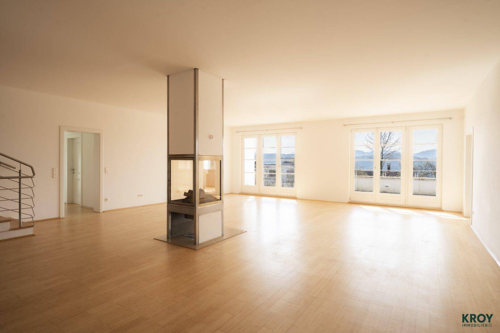 Geräumiges, helles Wohnzimmer mit Holzboden, modernem Kamin und Zugang zu einer Terrasse.